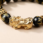 Black obsidian Pixiu bracelet close-up: gold-tone Pixiu between mantra-carved obsidian beads and gold dice