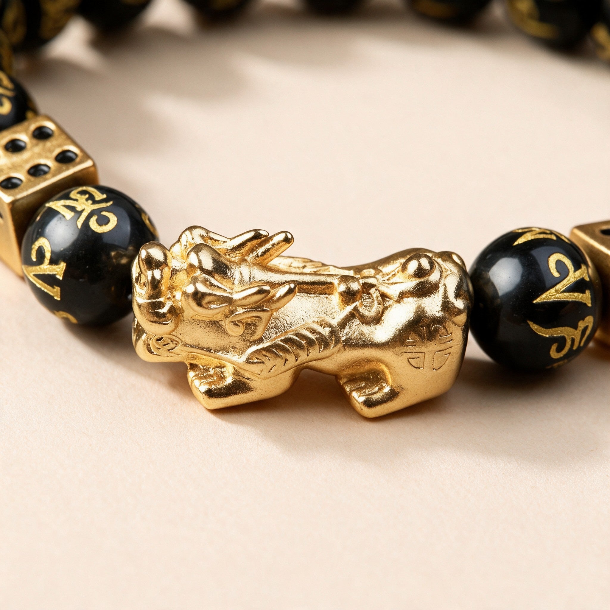 Black obsidian Pixiu bracelet close-up: gold-tone Pixiu between mantra-carved obsidian beads and gold dice