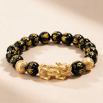 Feng Shui Pixiu black obsidian bracelet full view: gold-tone Pixiu, gold carved spacer beads and mantra-carved 10mm obsidian beads