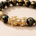 Feng Shui Pixiu bracelet close-up: gold-tone Pixiu between mantra-carved black obsidian beads
